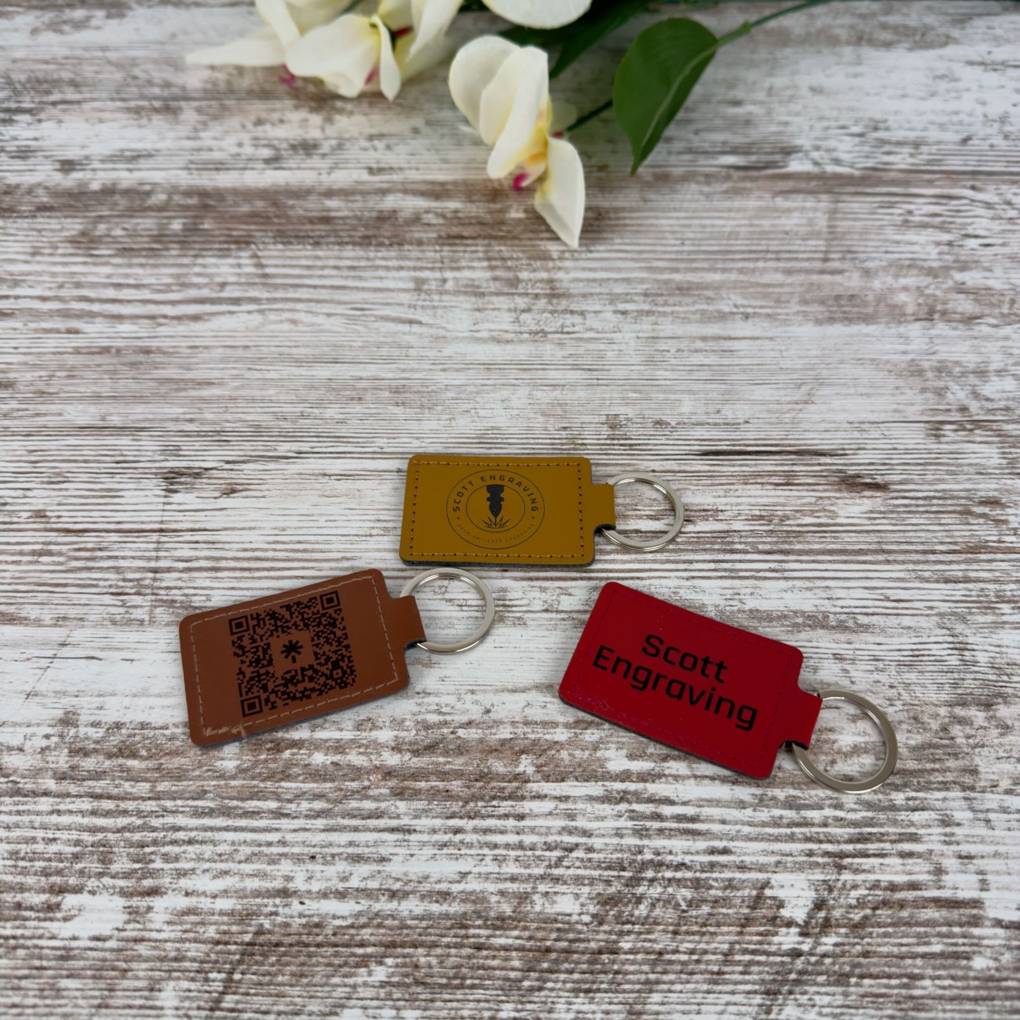 Three personalized leatherette keychains on a wooden surface 
